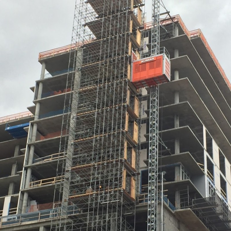 Tall construction hoist and supported scaffolding on a multi-story concrete building under construction
