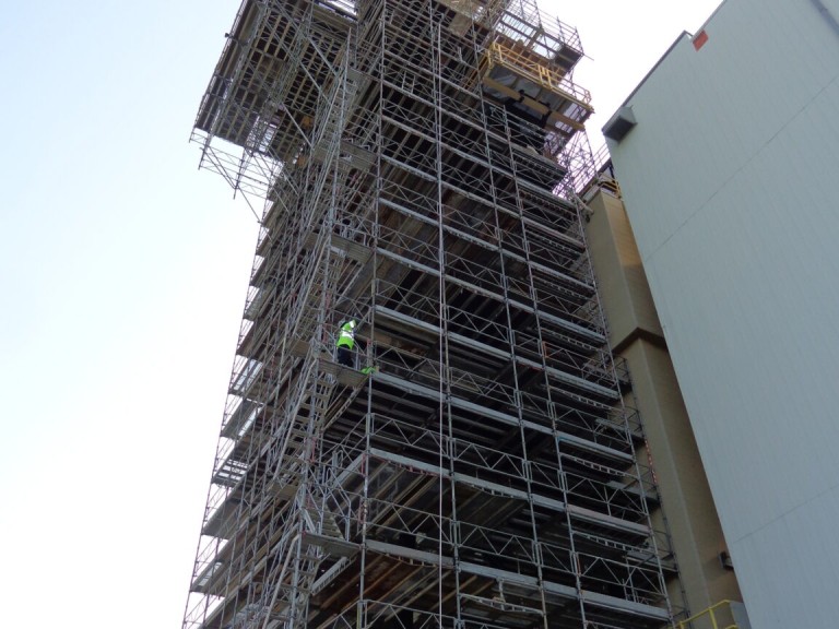 High-rise industrial building surrounded by extensive supported scaffolding with worker in safety gear
