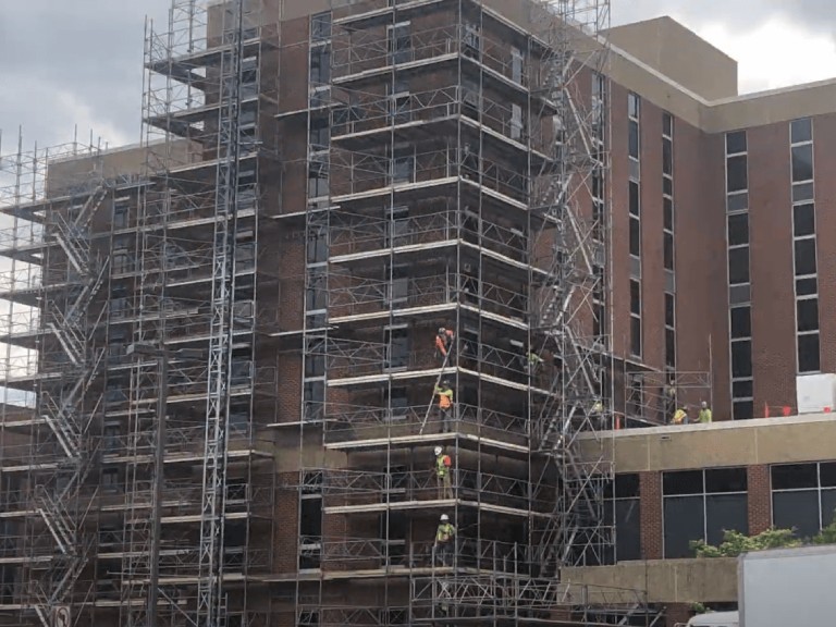 Construction workers on a large supported scaffolding system around a multi-story brick building