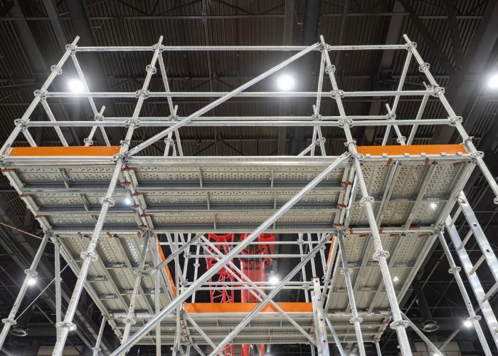 Metal scaffolding structure set up inside a building with bright lights overhead.