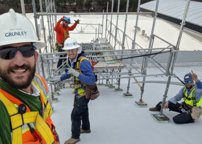 Scaffolding crew smiling and posing safely while working on a rooftop construction project.