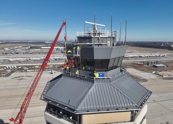 Technicians conducting high-altitude repairs on an airport control tower using scaffolding and crane equipment.