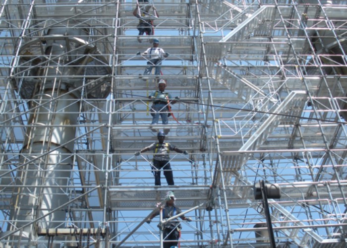 Maintenance crew climbing multi-level scaffolding for exterior inspection and repair work on an industrial structure.