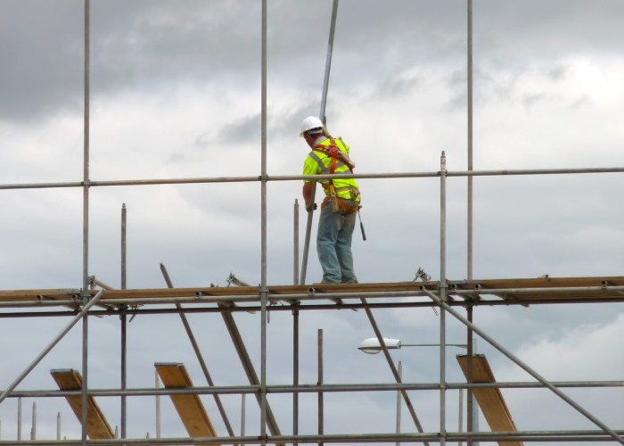 Worker in a safety harness installing scaffolding components at height on a construction project.
